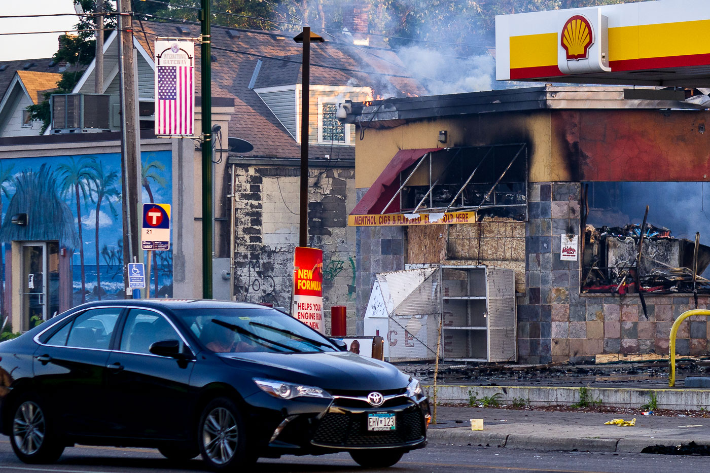 Car drives in front of burning shell gas station