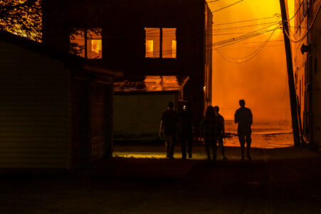 People walking down an alley as fires burn across the street during the 2nd day of protests in Minneapolis following the death of George Floyd.
