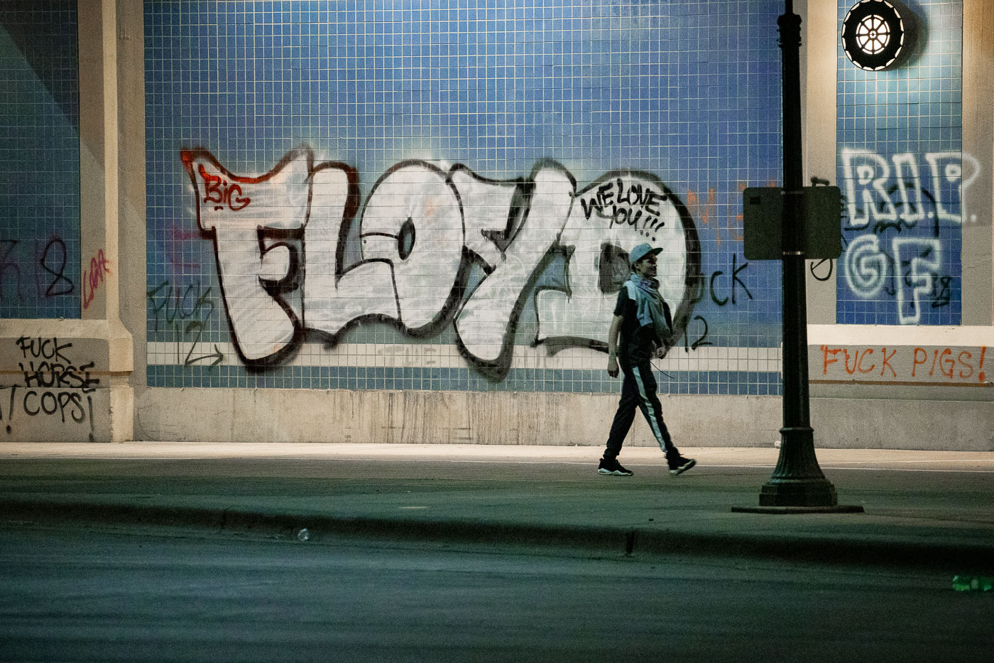 Man walks under Haiwatha Ave with FLOYD graffiti on wall