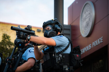 A Minneapolis Police officer aiming his less lethal weapon outside the Minneapolis Police 3rd Precinct on the second day of protests.