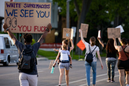 Protester holds up a sign reading “White supremacists We See You… you fucks” as they march down Park Avenue into downtown Minneapolis.