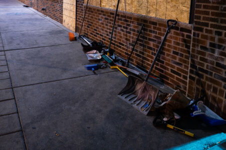 Brooms and shovels on the side of a building for community cleanup of damaged buildings during civil unrest in Minneapolis.