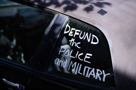 A car with “Defund the police and military” written on a window.