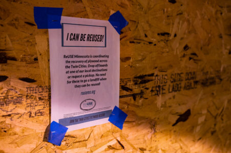 ReUSE Minnesota flyer on storefront board. The organization is coordinating the recovery of plywood across the twin cities after it was used to cover doors and windows.