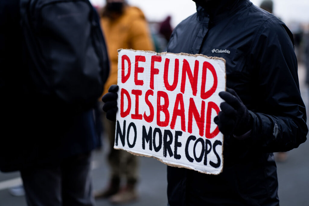 A woman holds up a sign that reads "Disfund Disband No More Cops" outside the Brooklyn Center Police Department.