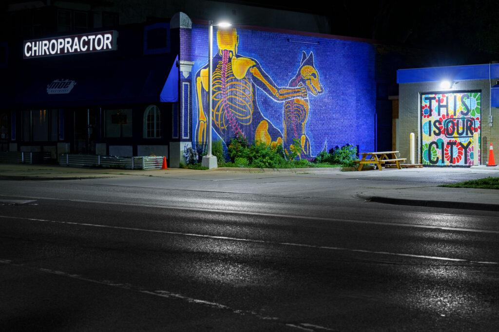 A mural on the side of a chiropractor's office in Minneapolis. "This Is Our City" written on boards at the gas station next door.