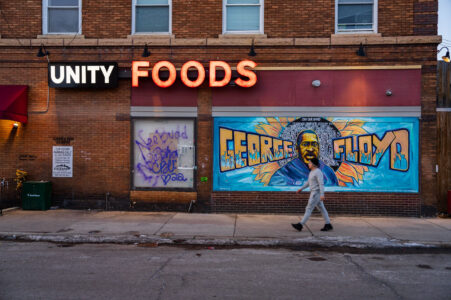 A man walks in front of the George Floyd mural on the side of "Unity Foods". Unity Foods was formerly named Cup Foods.