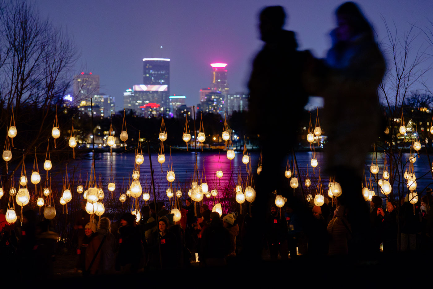A couple walk in front of luminaries with city skyline
