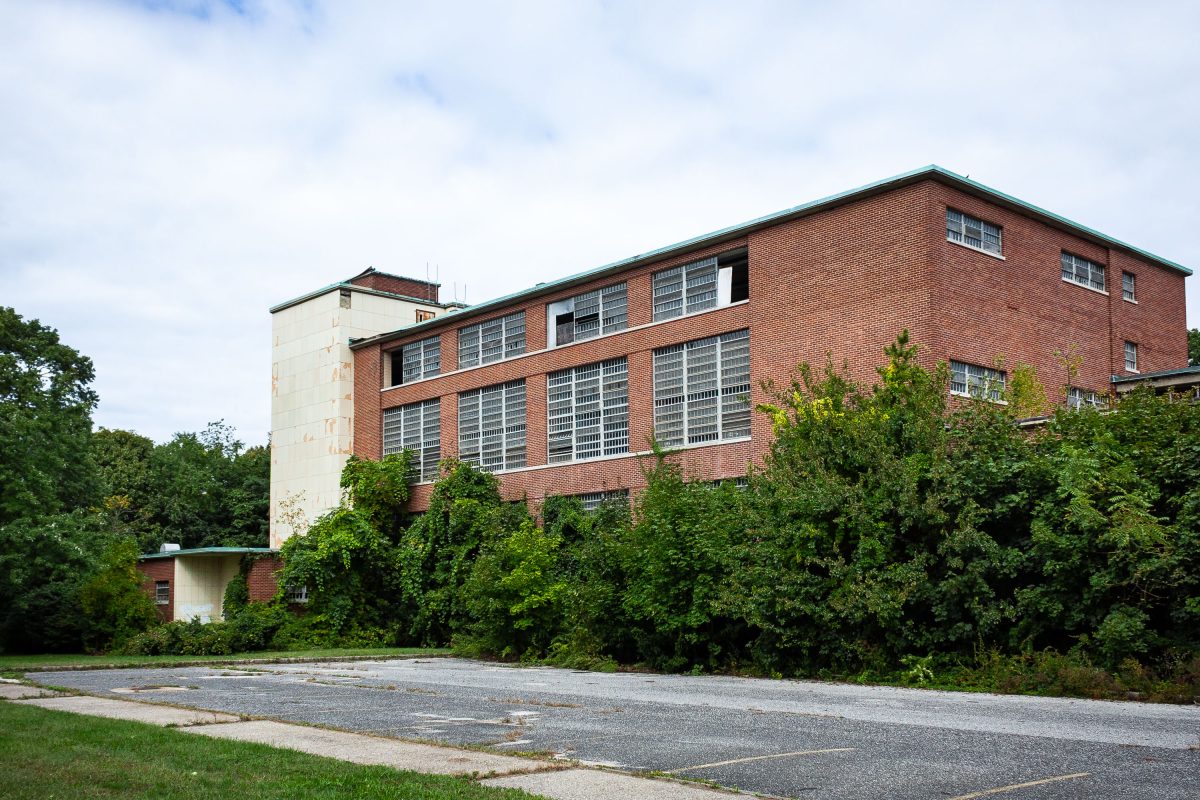 Brick institutional building with barred windows and dense overgrown vegetation at Kings Park Psychiatric Center, New York.