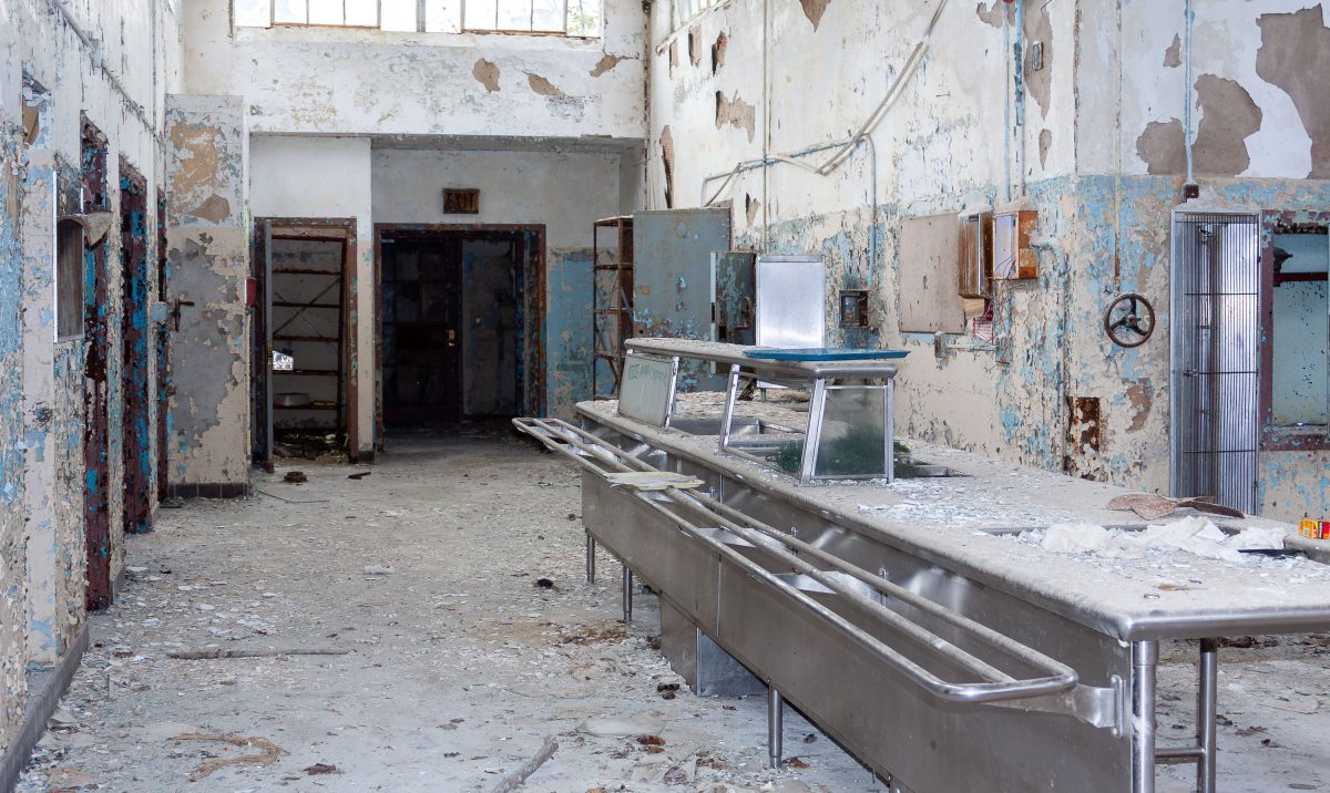 Abandoned institutional kitchen with peeling blue paint, metal counters, and deteriorating doorways at Kings Park Psychiatric
