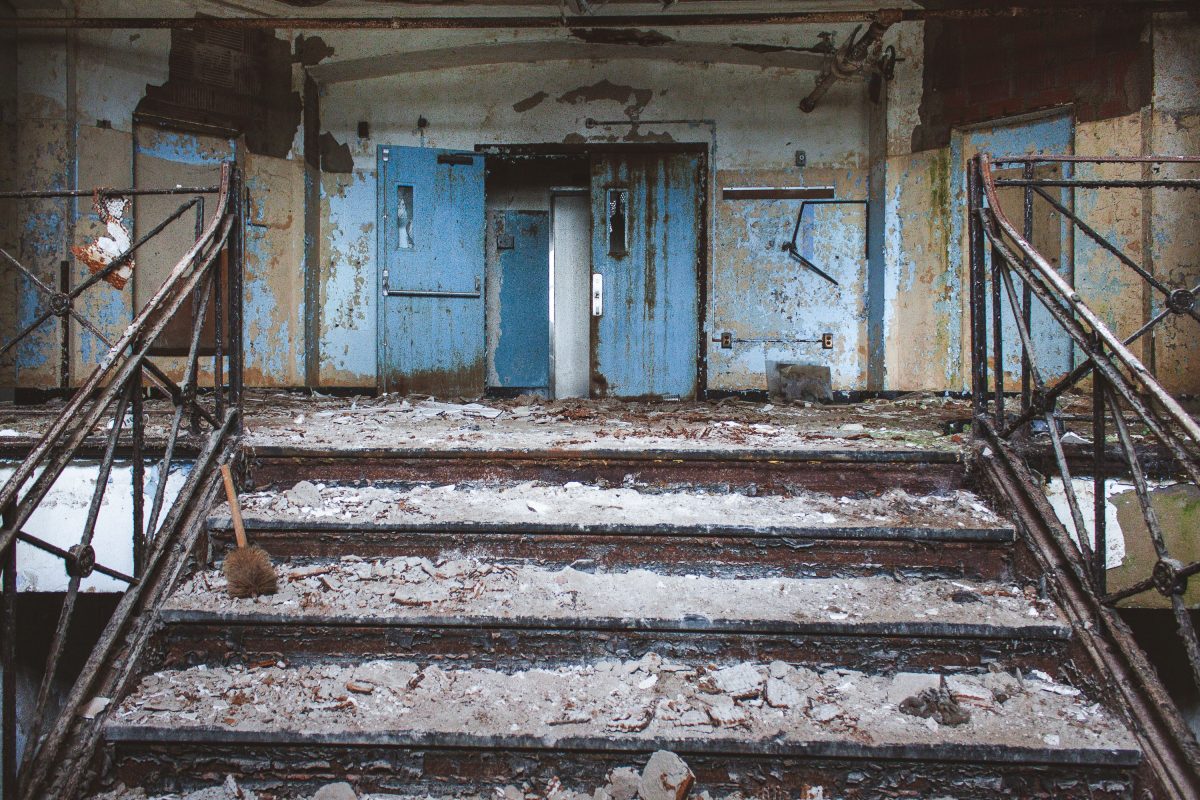 Deteriorated staircase with peeling blue paint and metal railings in abandoned Kings Park Psychiatric Center.