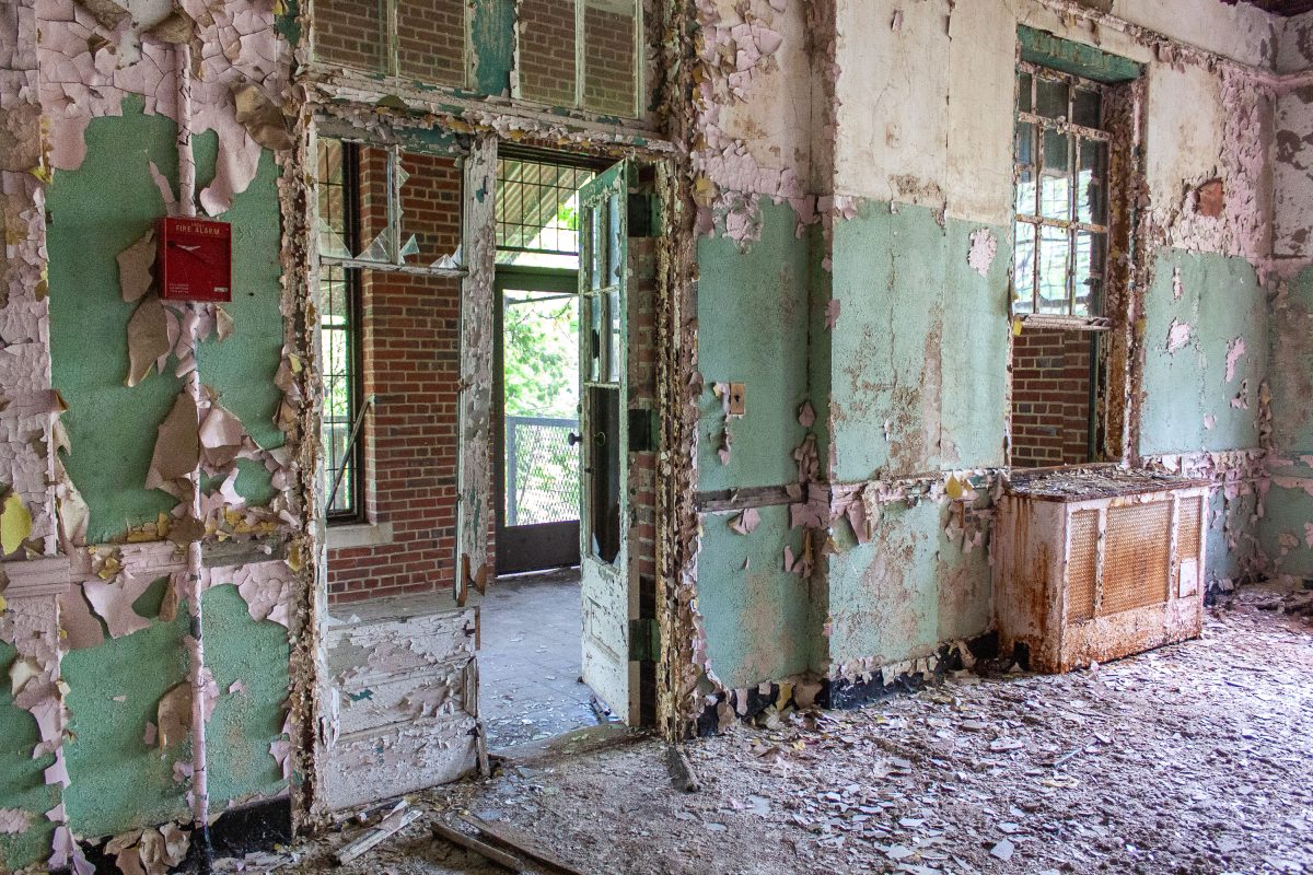 Deteriorated hallway with peeling green paint and open doorways in abandoned Kings Park Psychiatric Center.