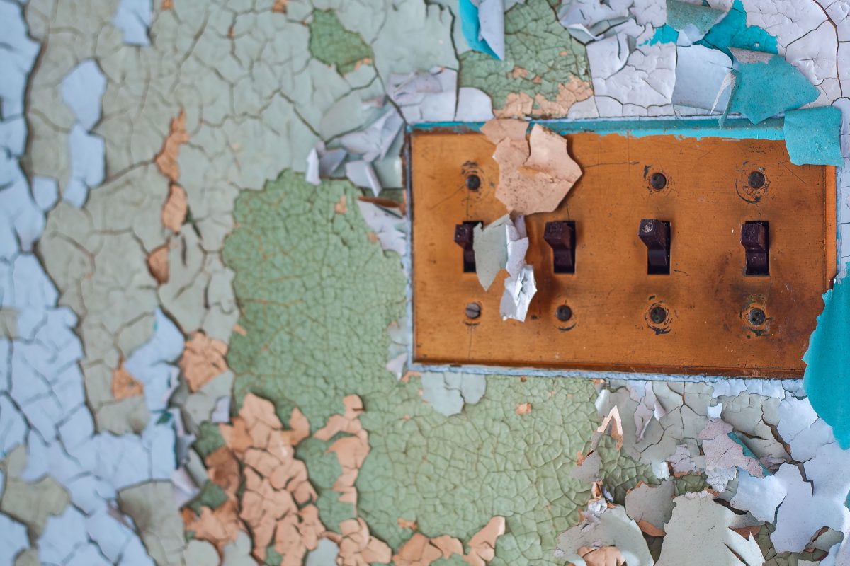 Deteriorating copper light switch plate on peeling wall at abandoned Kings Park Psychiatric Center, New York.
