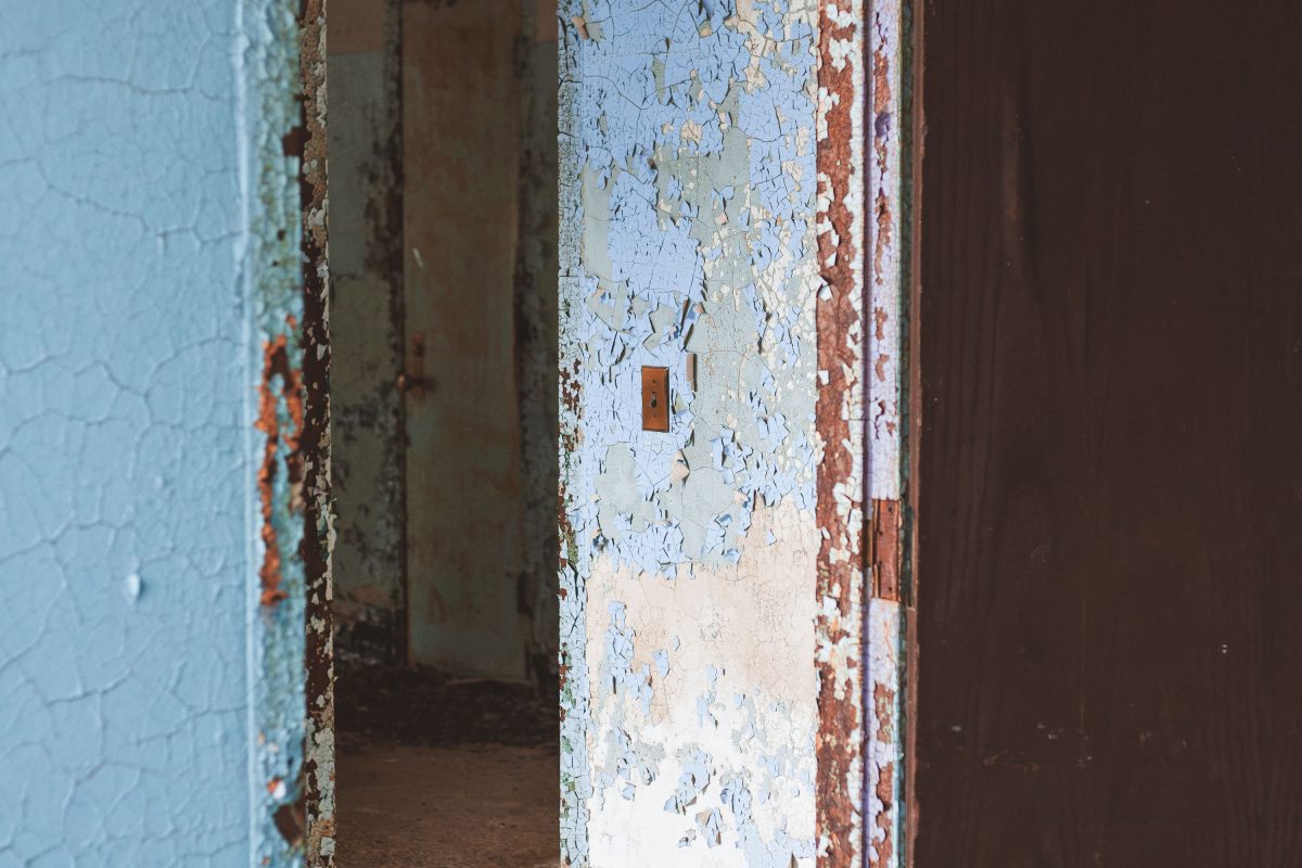 Deteriorated hallway with peeling blue and white paint and open doorways at Kings Park Psychiatric Center.