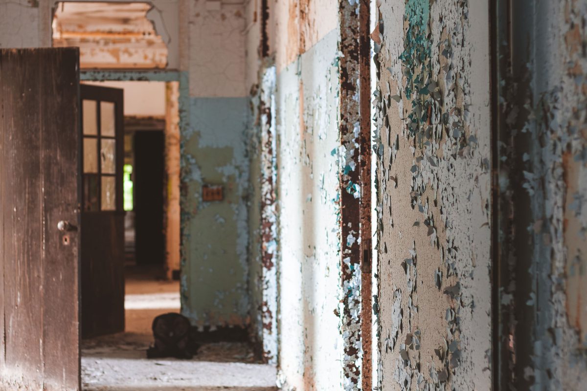 Deteriorated hallway with peeling paint and open doorways in abandoned Kings Park Psychiatric Center.