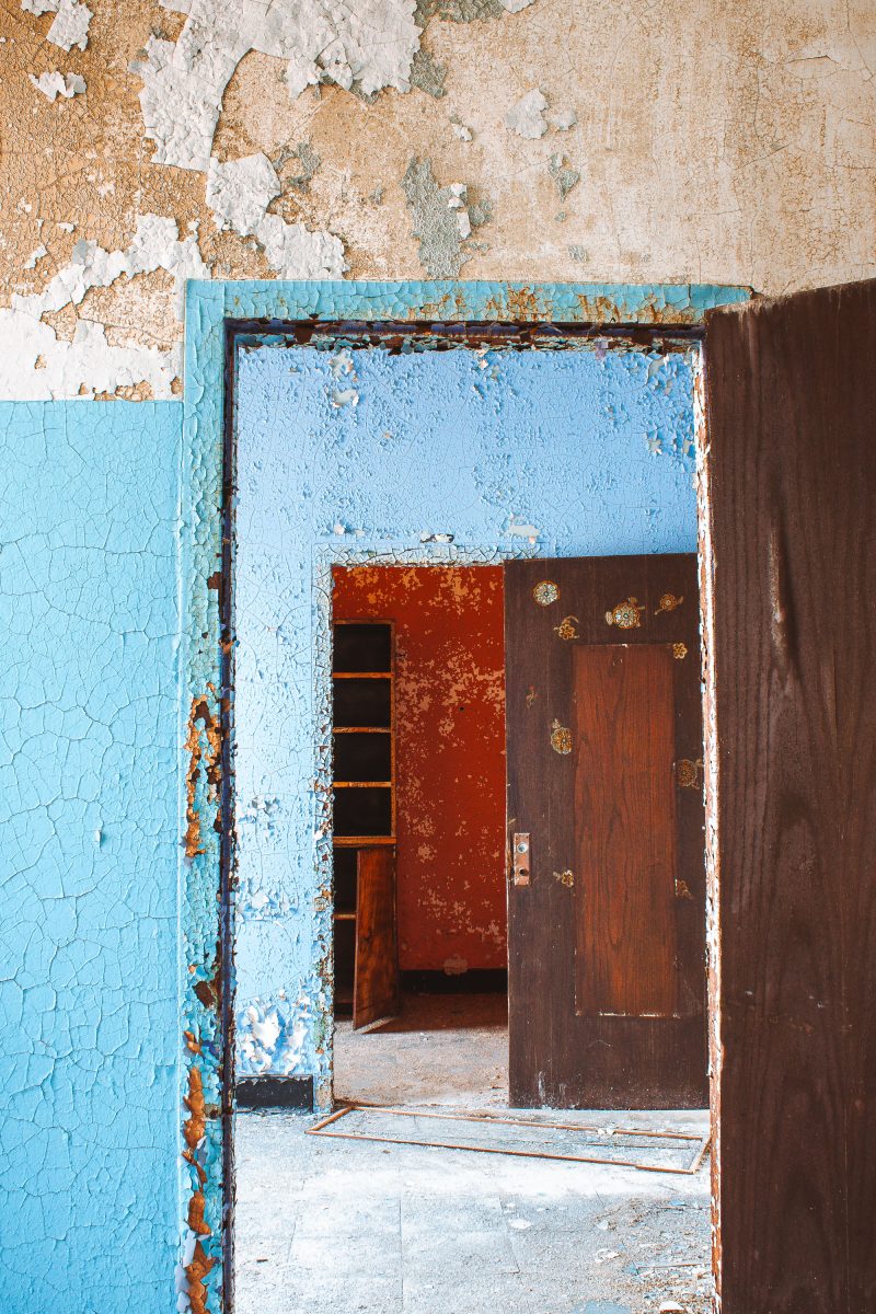 Deteriorating doorway with peeling blue and red paint at Kings Park Psychiatric Center, New York.