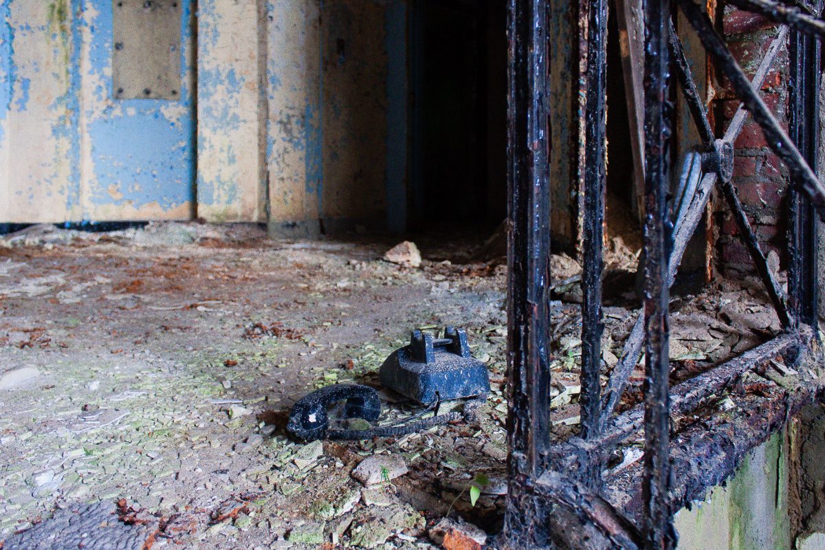 Deteriorated courtyard floor with abandoned blue metal fixture and rusted iron gate at Kings Park Psychiatric Center.