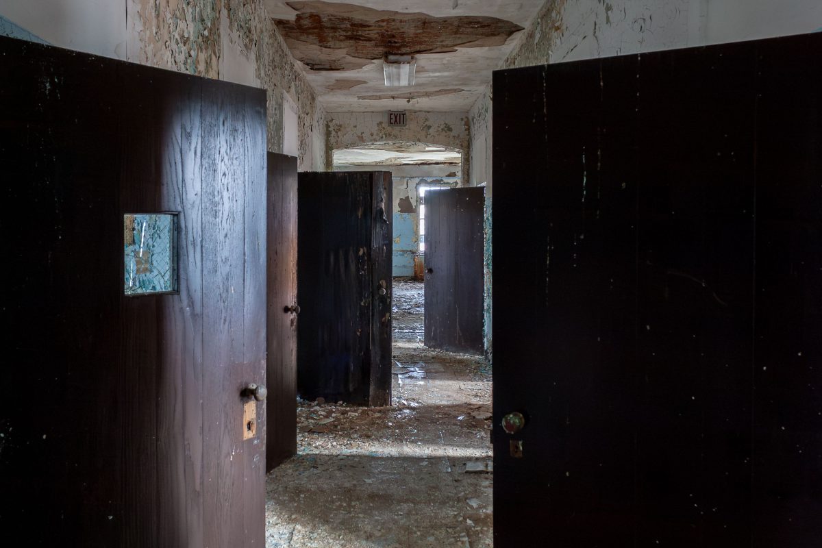 Deteriorated hallway with dark wooden doors and peeling walls in abandoned Kings Park Psychiatric Center, New York.