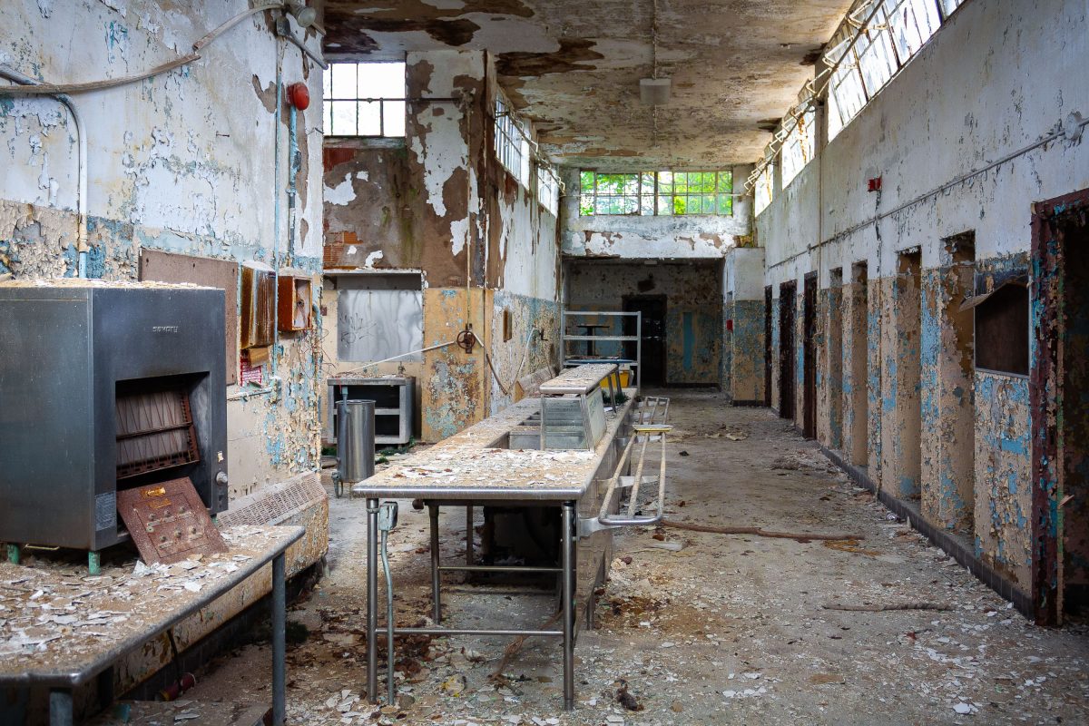 Abandoned institutional cafeteria with deteriorated walls, metal tables, and peeling paint at Kings Park Psychiatric Center.