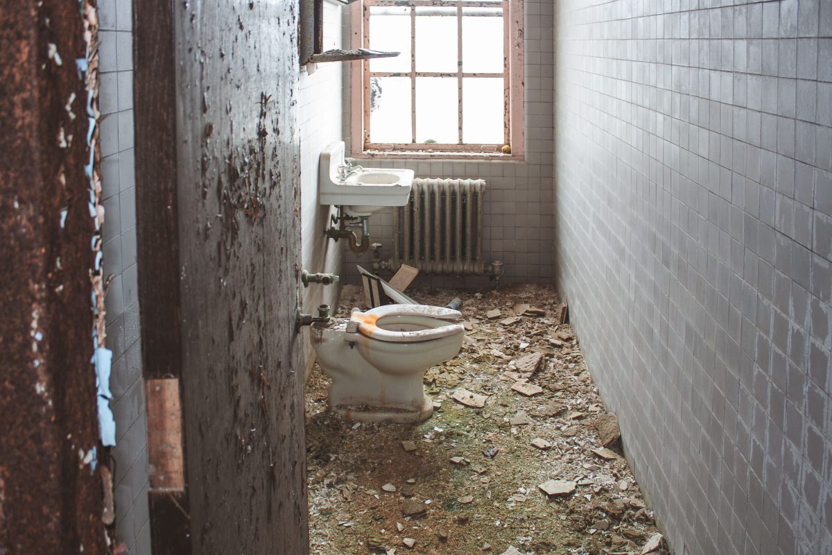 Abandoned bathroom with deteriorated walls, toilet, sink, and radiator at Kings Park Psychiatric Center.