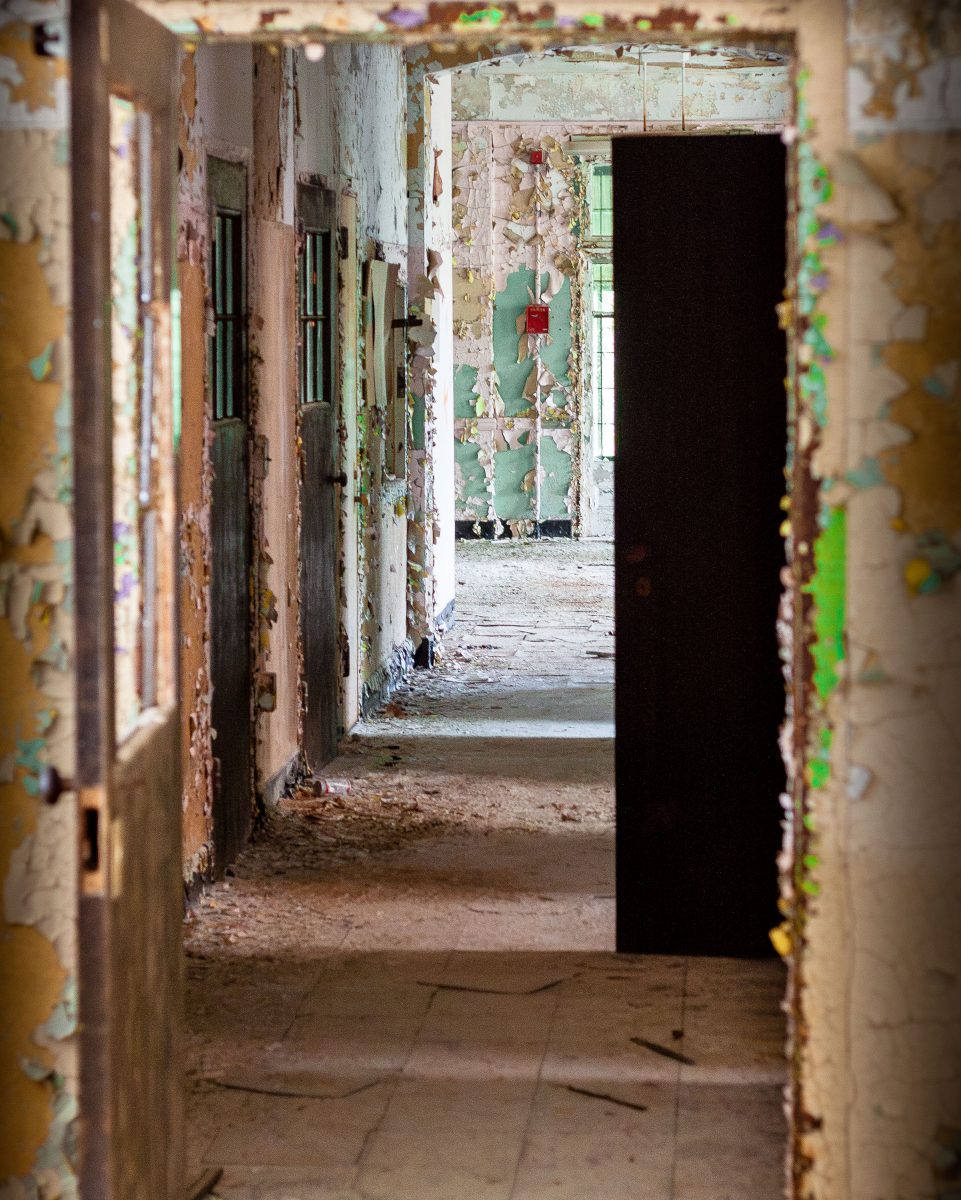 Deteriorated corridor with peeling paint and open doorways in abandoned Kings Park Psychiatric Center, New York.