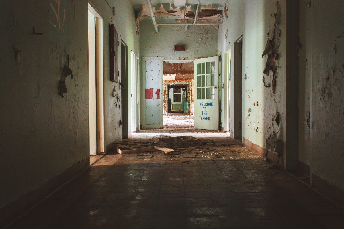 Deteriorated hallway in abandoned Kings Park Psychiatric Center with peeling walls and "Welcome to the Threes" text visible on