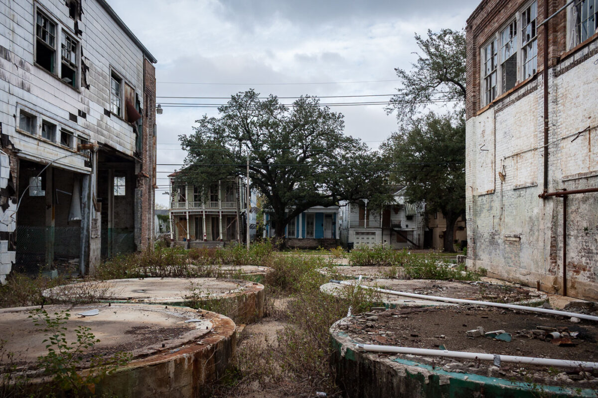 Abandoned concrete tanks at the former Dixie Brewery in New Orleans, surrounded by overgrown vegetation and derelict industrial buildings.