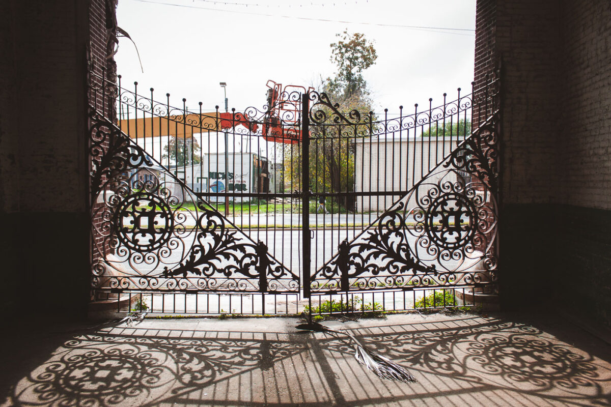 The ornate wrought-iron gates of the former Dixie Brewery in New Orleans, a historic landmark, stand open, with building text visible.