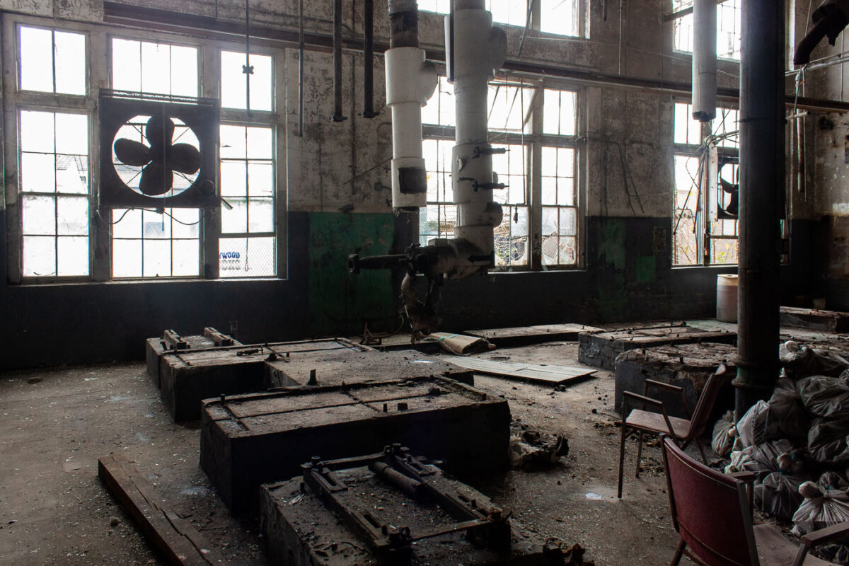Interior of the abandoned Dixie Brewery in New Orleans, showing industrial machinery, concrete vats, and debris. A sign reads "WOOD."