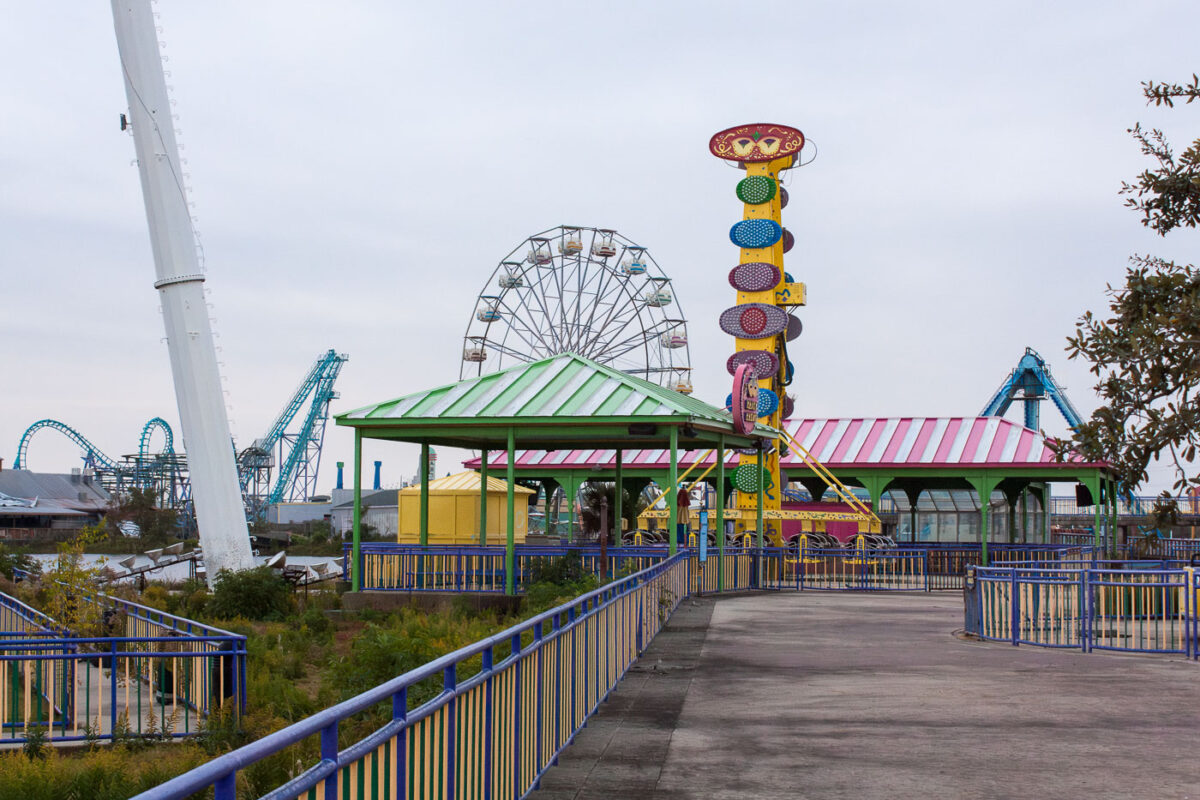 The abandoned Six Flags New Orleans amusement park, damaged by Hurricane Katrina, stands empty with overgrown vegetation encroaching on pathways and structures.