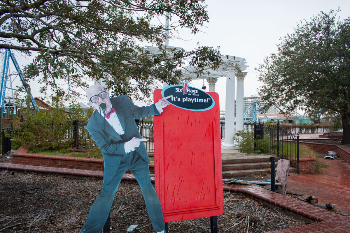 Six Flags New Orleans amusement park, closed after Hurricane Katrina, shows a cardboard cutout figure and dilapidated roller coasters under a cloudy sky.