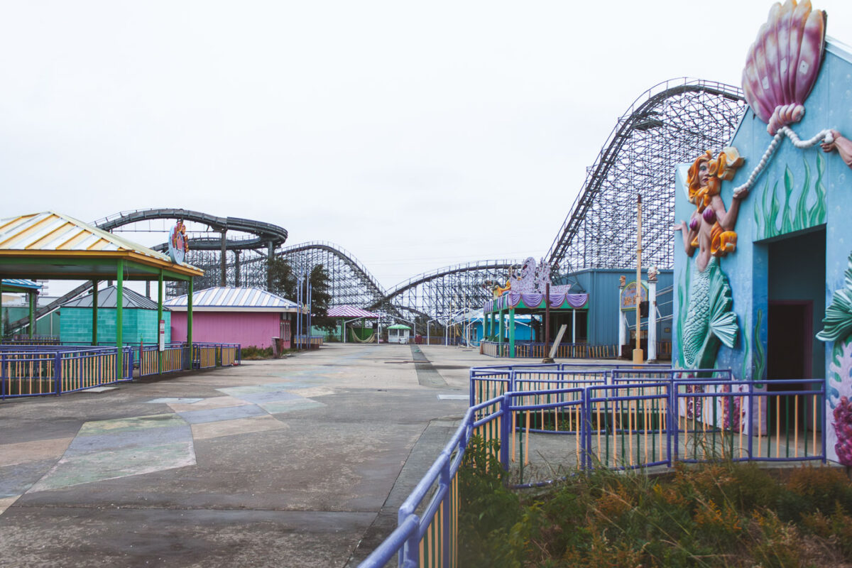 The abandoned Six Flags New Orleans amusement park, damaged by Hurricane Katrina, shows a large wooden roller coaster and faded whimsical structures.