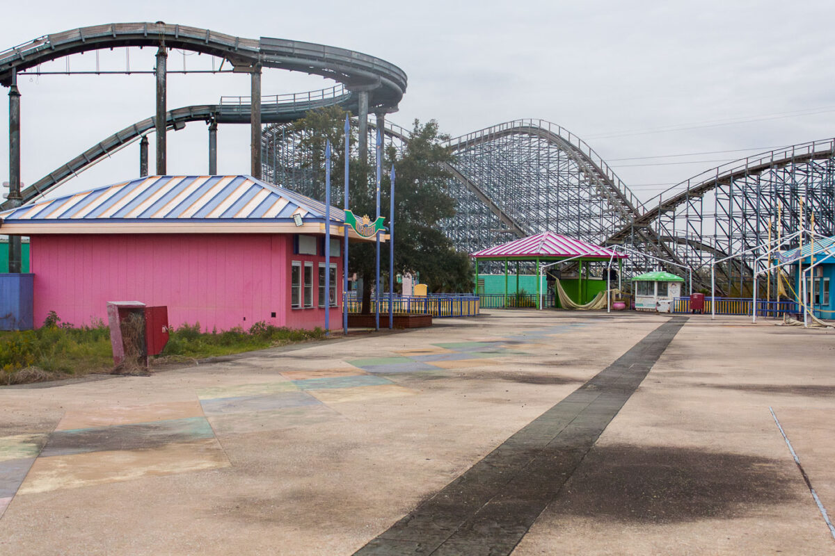 The abandoned Six Flags New Orleans amusement park shows extensive damage and decay after Hurricane Katrina, with overgrown vegetation and rusted roller coaster tracks.
