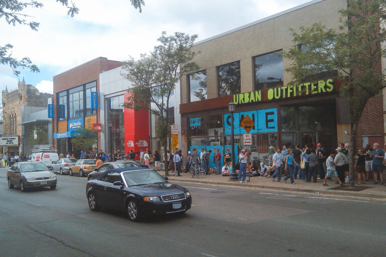 Apple Store Opens in Uptown Minneapolis 3 Crowds line Uptown Minneapolis sidewalk outside an Apple Store opening, with Urban Outfitters beside it.