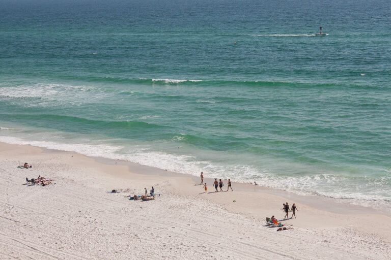 Beach goers walking in Panama City Beach 4 People lay and walk on the beach in Panama City Beach, Florida.