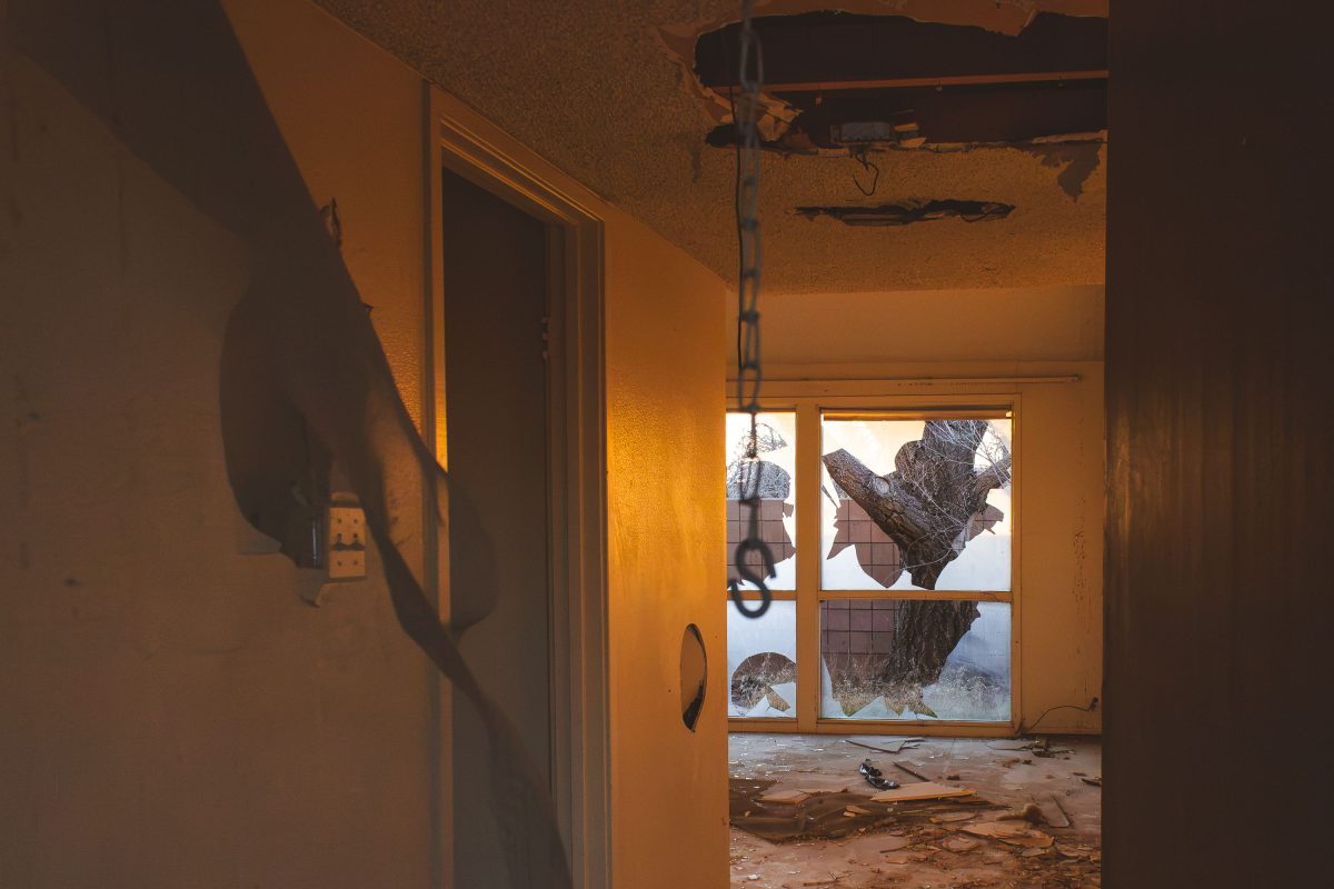 Interior of abandoned residential building at George Air Force Base showing orange-lit room with bare tree visible through broken