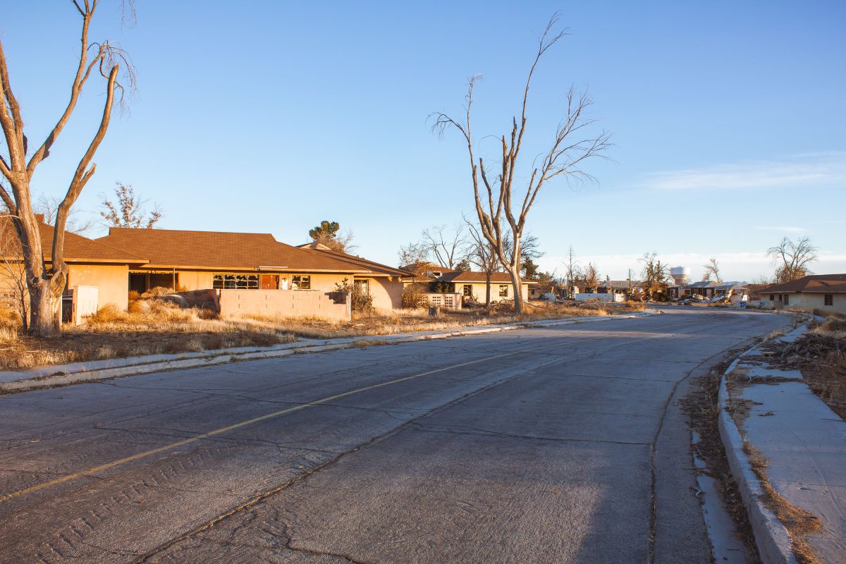 Abandoned residential building with bare trees along cracked pavement at George Air Force Base in Victorville, California.