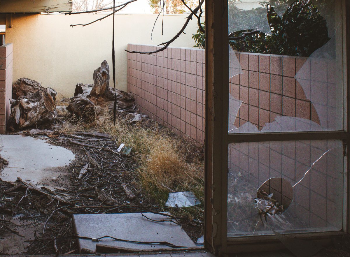 Deteriorated interior courtyard with debris and bare branches visible through broken glass doors at George Air Force Base.