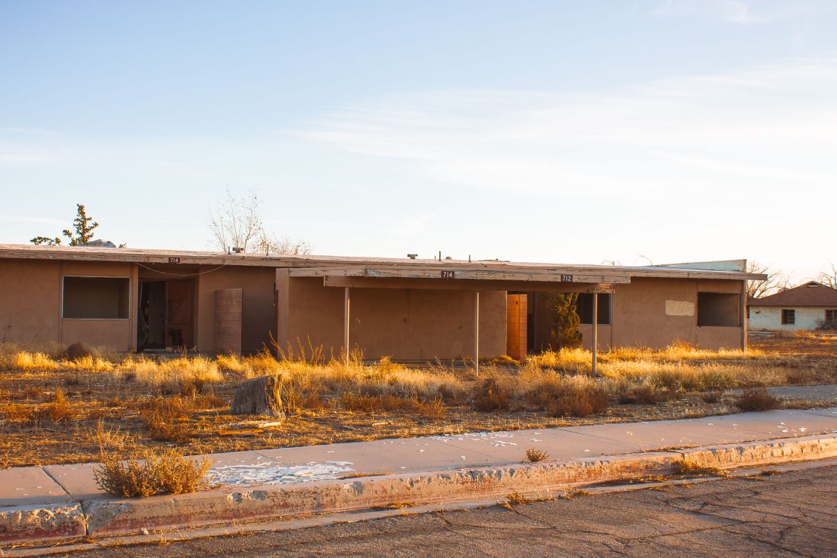 Abandoned residential building with broken windows and dry vegetation at George Air Force Base in Victorville, California.