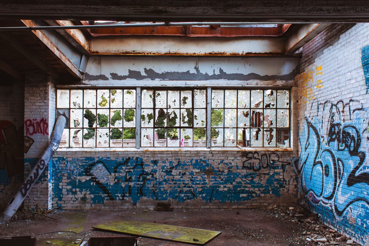 Abandoned Fruen Mill interior in Minneapolis with broken windows, peeling paint, and blue graffiti on brick walls.