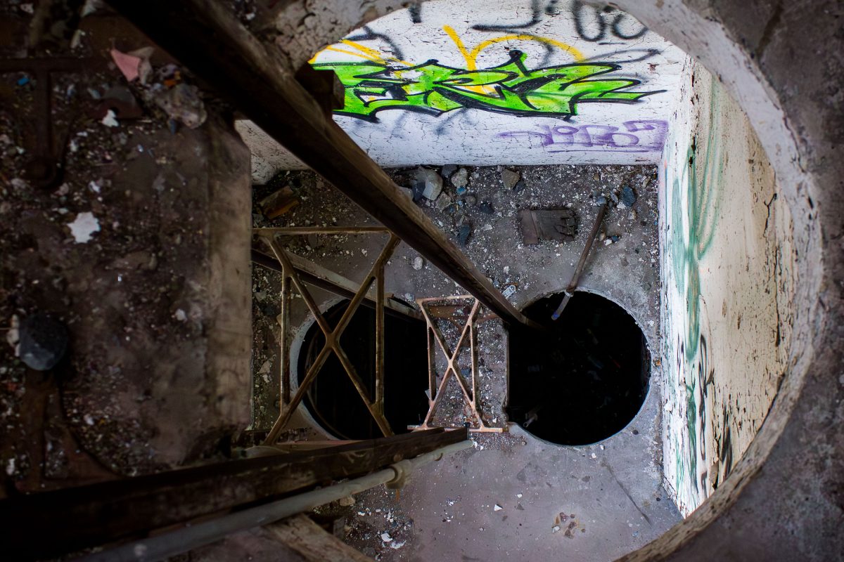 Graffiti-marked concrete ceiling and rusted metal staircase inside the abandoned Fruen Mill grain processing facility in