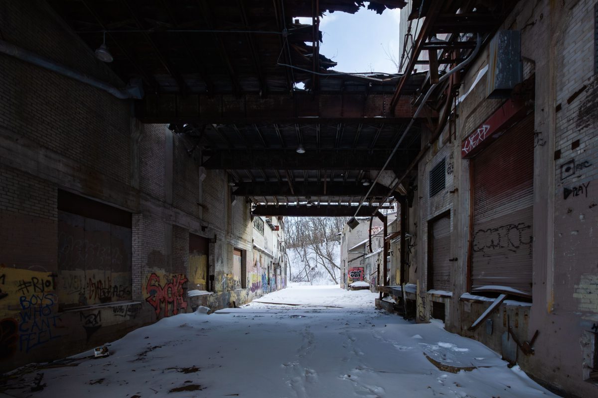 Abandoned Fruen Mill industrial corridor in Minneapolis with snow-covered ground, brick walls, and graffiti.