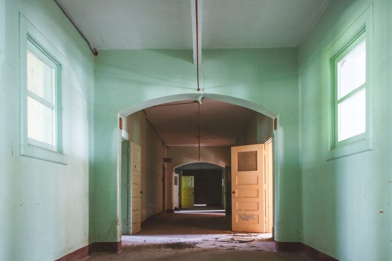 Arched corridor with green walls, Fergus Falls Kirkbride Building 3 Abandoned institutional hallway with mint green walls, wooden doors, and arched ceiling at Eagle Island psychiatric hospital.