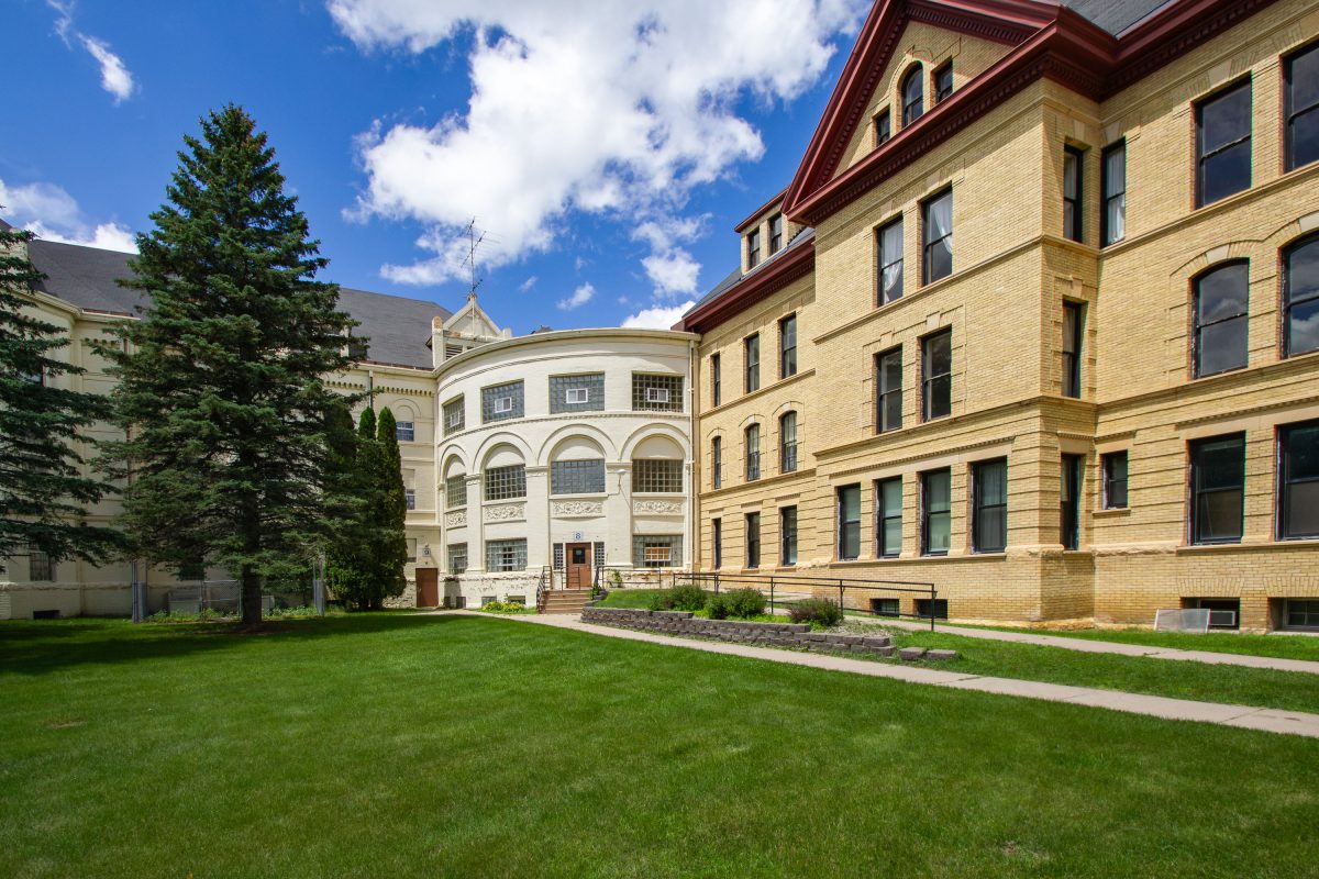 Kirkbride-designed psychiatric hospital building with curved wing and mansard roof on grassy campus in Fergus Falls, Minnesota.