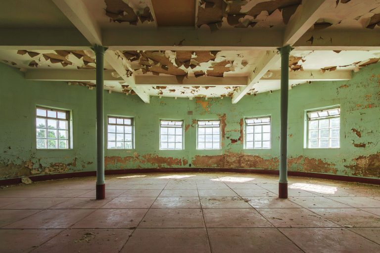 Curved Sunroom with Peeling Paint, Fergus Falls Kirkbride Building 4 Abandoned institutional gymnasium with peeling green walls, exposed ceiling damage, and support columns at Eagle Island in Fergus