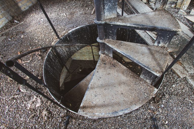 Descending Spiral Staircase, Fergus Falls Kirkbride Building, Minnesota 1 Overhead view of an abandoned spiral staircase with metal railings descending into darkness at Eagle Island.