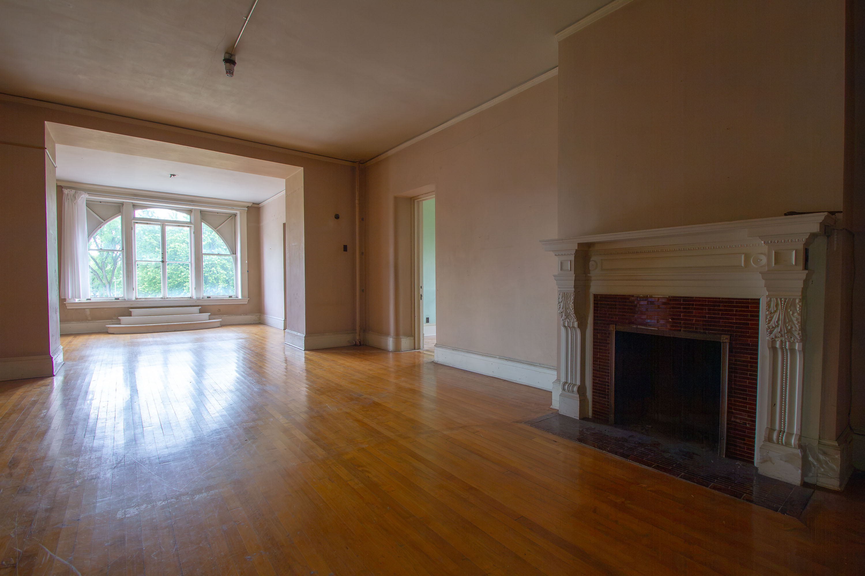Empty residential room with hardwood floors, fireplace, and bay window at Eagle Island, Fergus Falls.