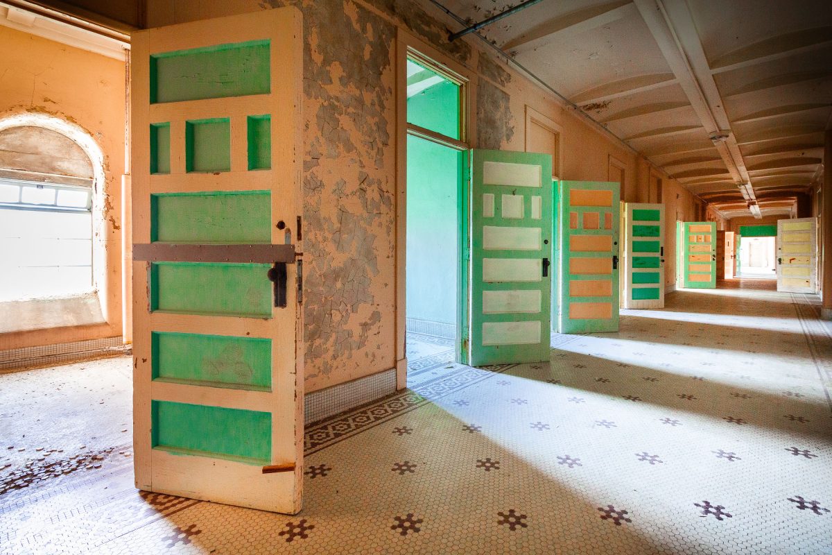 Row of green ward doors along hexagonal-tile corridor, Fergus Falls Kirkbride Building