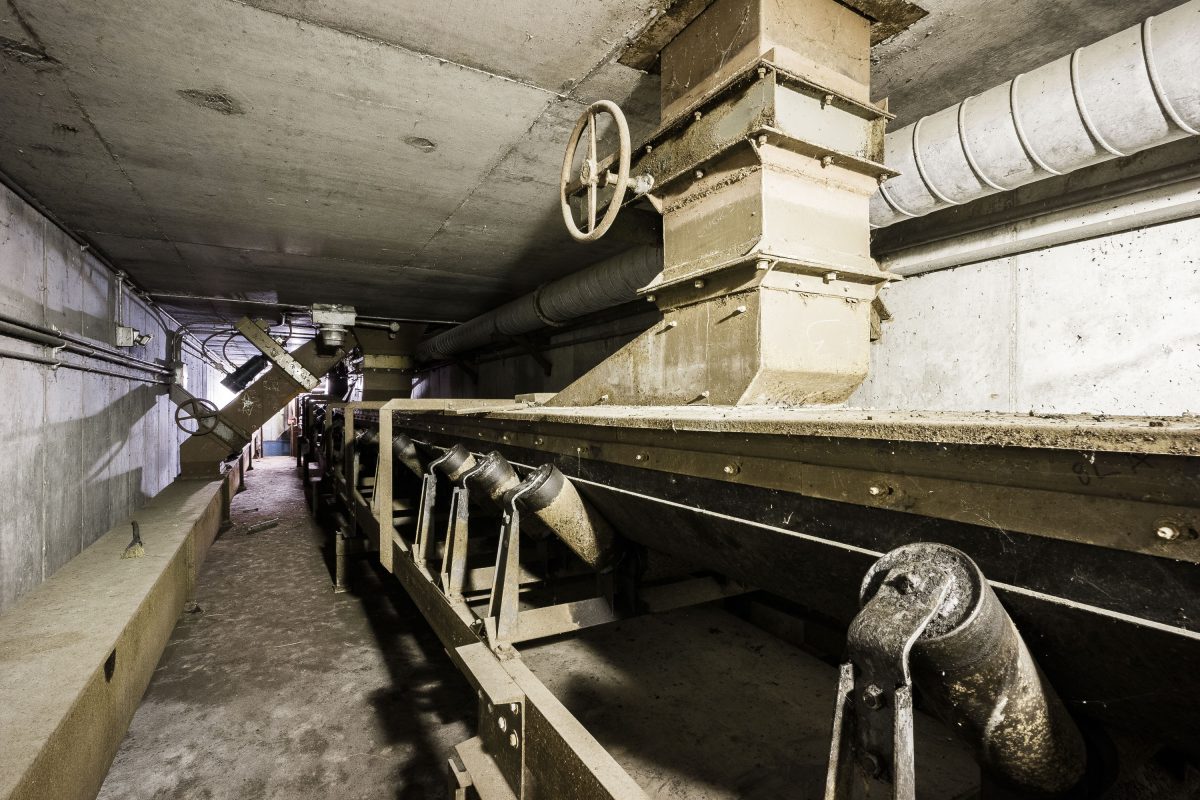 Interior of Upper Harbor Terminal showing industrial conveyor equipment, control valve, and metal infrastructure in the abandoned barge facility.