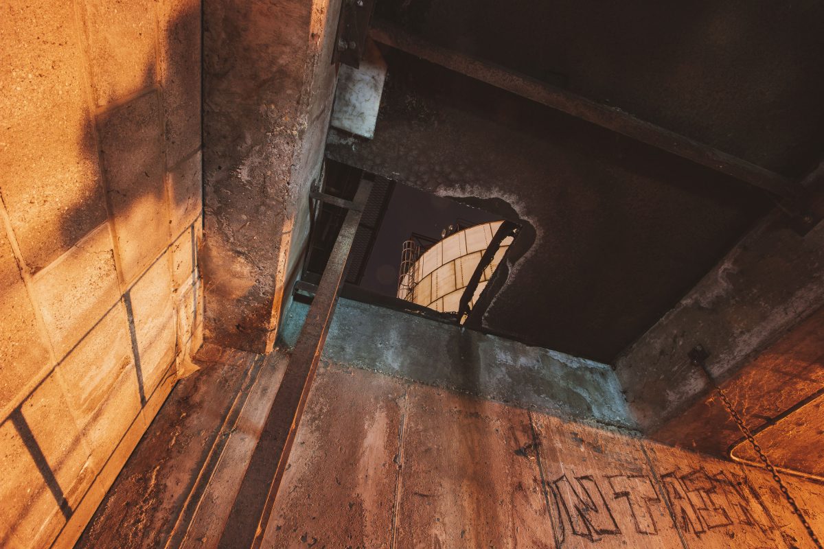 Rusted metal chair sits in sunlit upper floor window of abandoned Upper Harbor Terminal barge facility on Mississippi River.